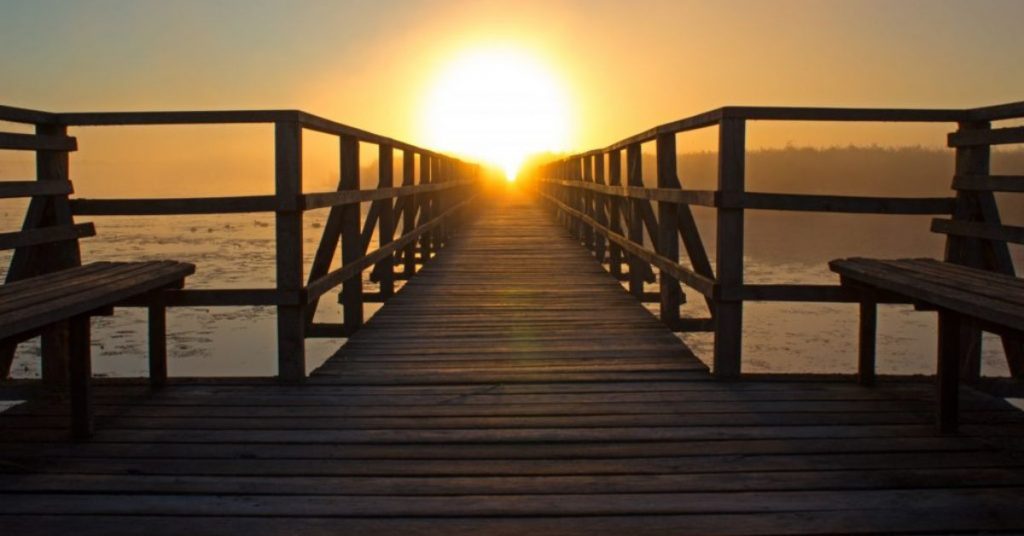 Looking out across a deck to the sea at the sun setting on the horidon