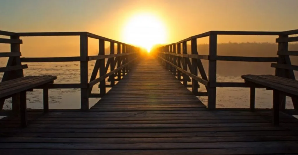 Looking out across a deck to the sea at the sun setting on the horidon