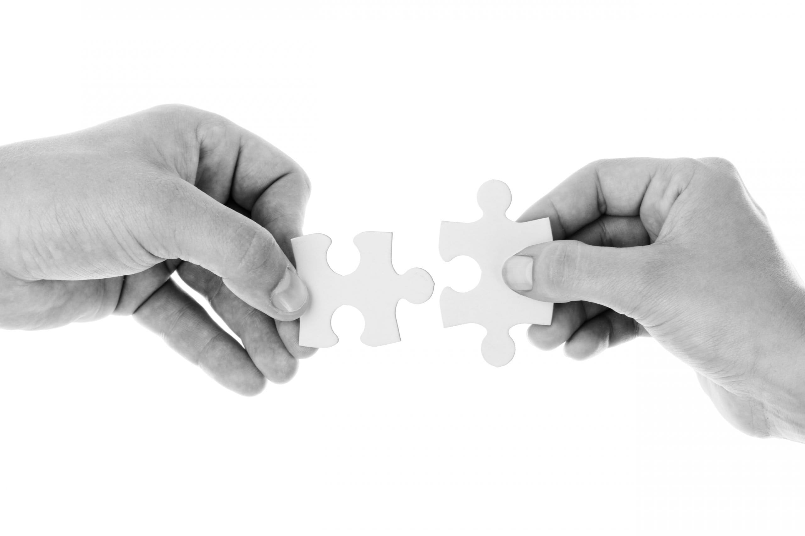 two hands holding white jigsaw pieces and bringing them together