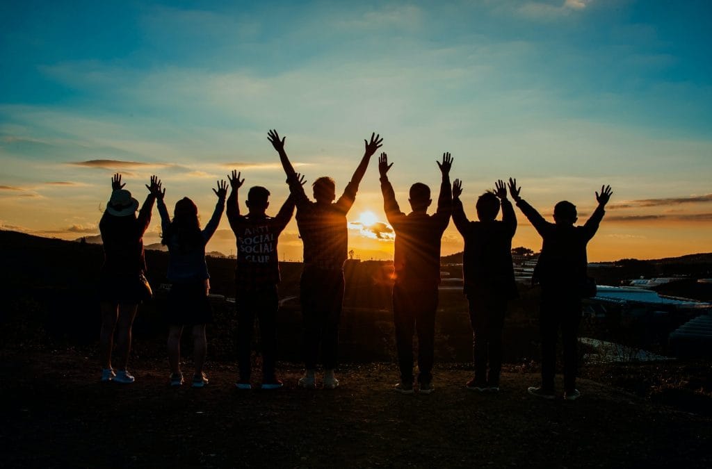 A team with upraised hands looking towards the sunset