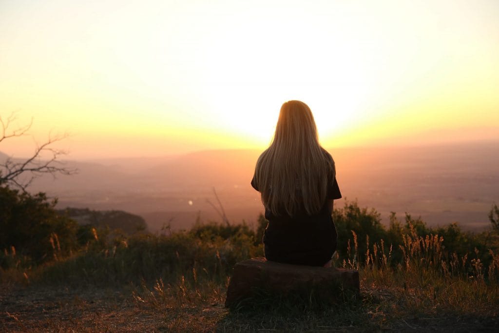 a girl sitting out in the open looking and thinking about the sunset