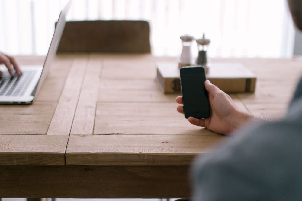a hand holding a mobile phoneover a desk