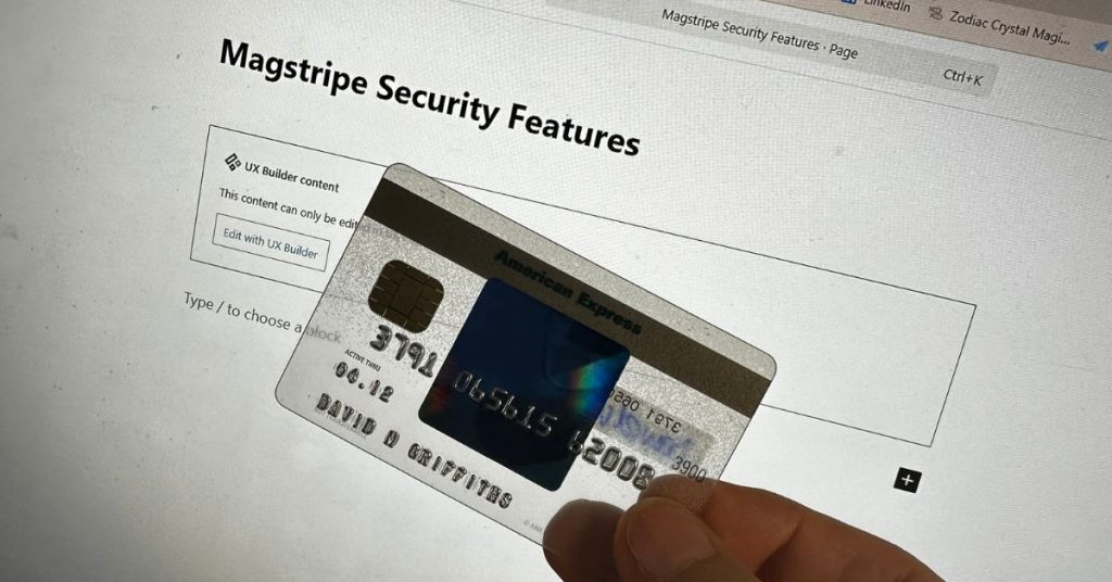 An American Express card being held between fingers and thumb, in front of a PC monitor to show magstripe security.